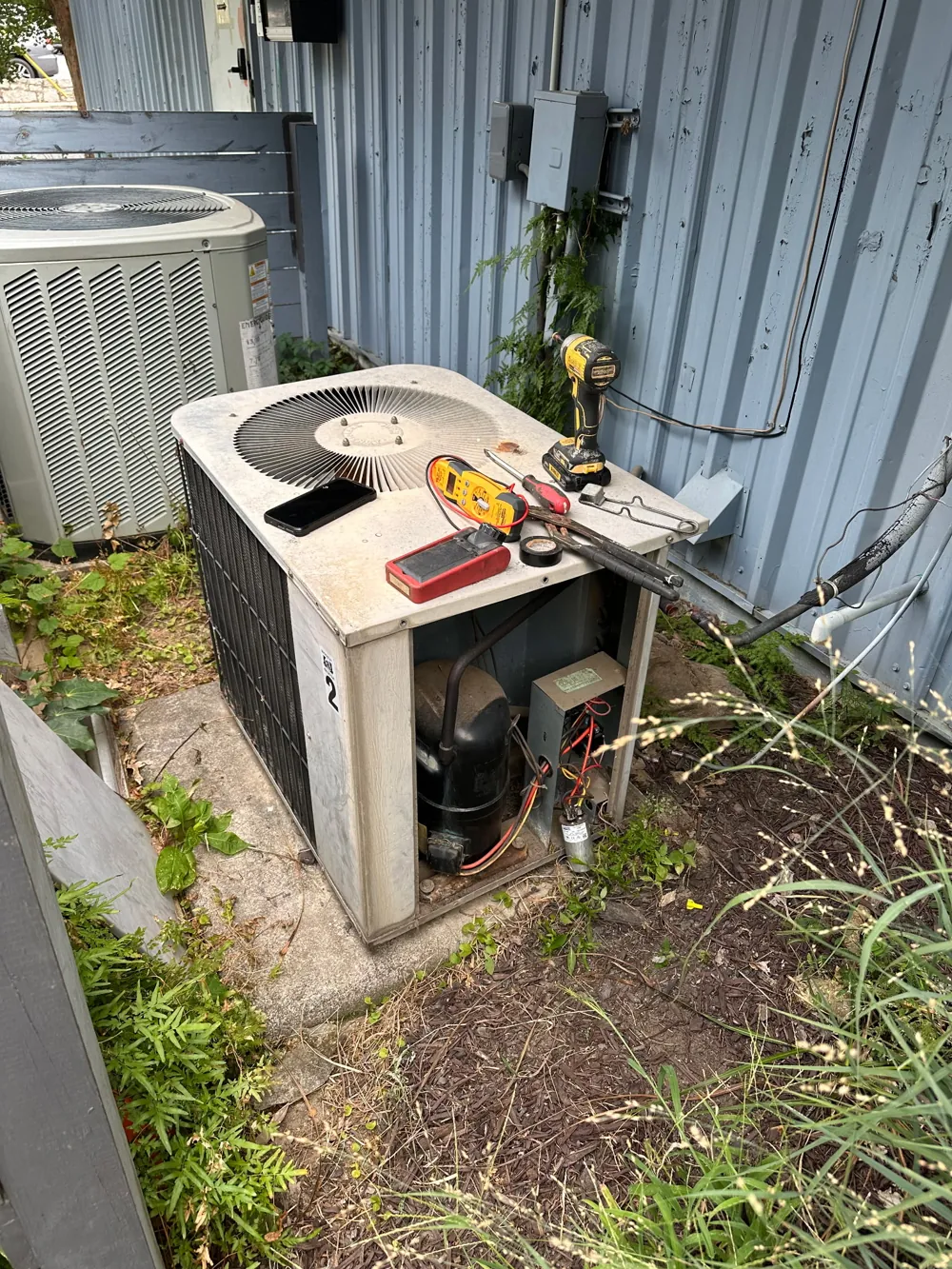Meter and tools resting on an open AC condenser during a diagnostic repair