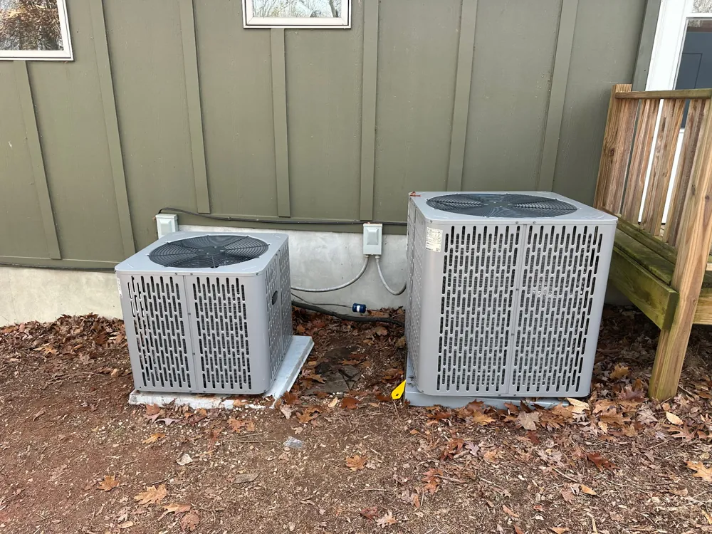 Two outdoor air conditioner condensers installed on pads beside a green-sided home